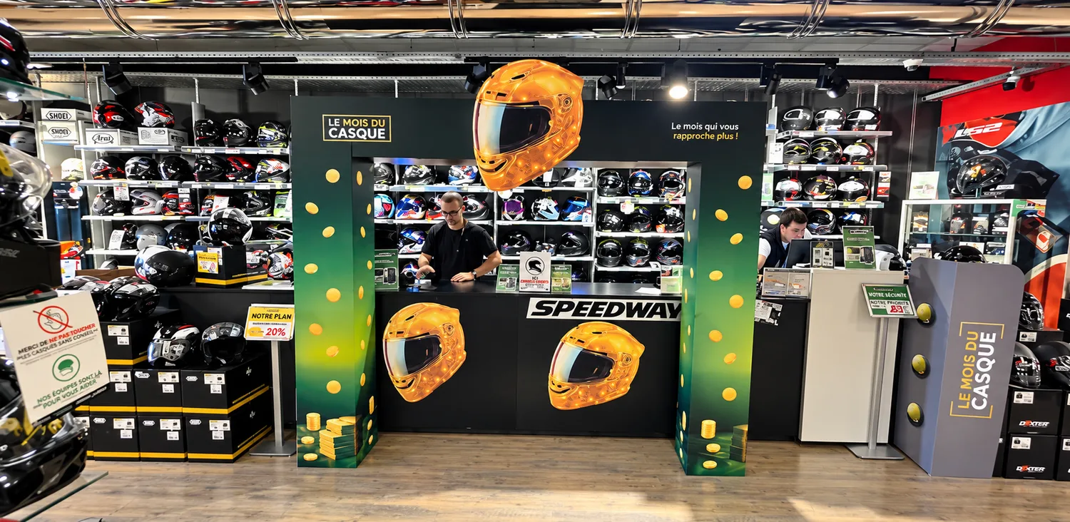 Arche Le Mois du Casque à l'entrée d'un magasin Speedway : deux piliers carton à dégradé vert et pièces d'or, bandeau supérieur et casque doré découpé, linéaire de casques en arrière-plan