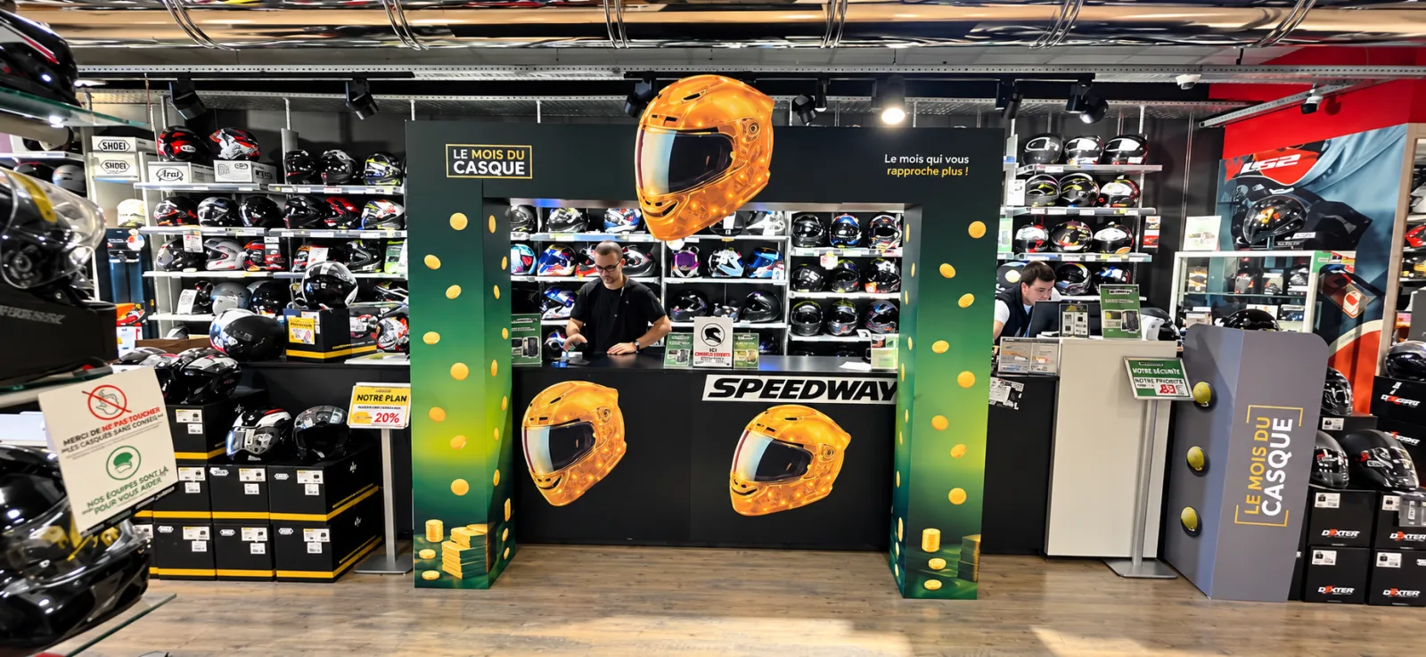 Arche Le Mois du Casque à l'entrée d'un magasin Speedway : piliers carton, bandeau et casque doré au-dessus du comptoir